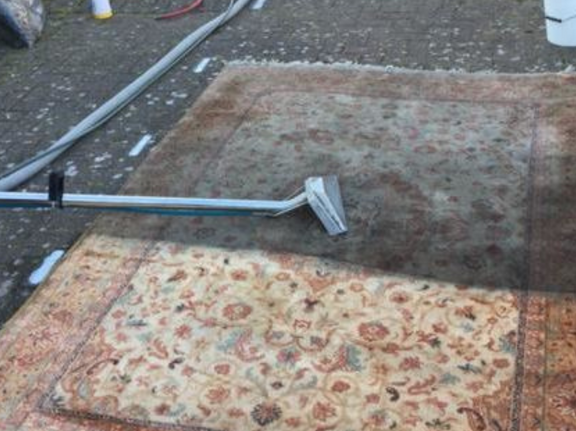 This is a photo of a floral rug that is being steam cleaned. The bottom half has been completed and the top half is being done works carried out by Rickmansworth Carpet Cleaning