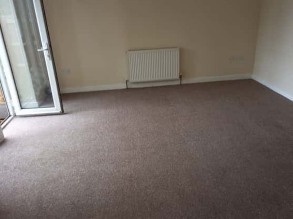 This is a photo of a living room after it has been cleaned. The room is empty and has a brown carpet that has been steam cleaned works carried out by Rickmansworth Carpet Cleaning